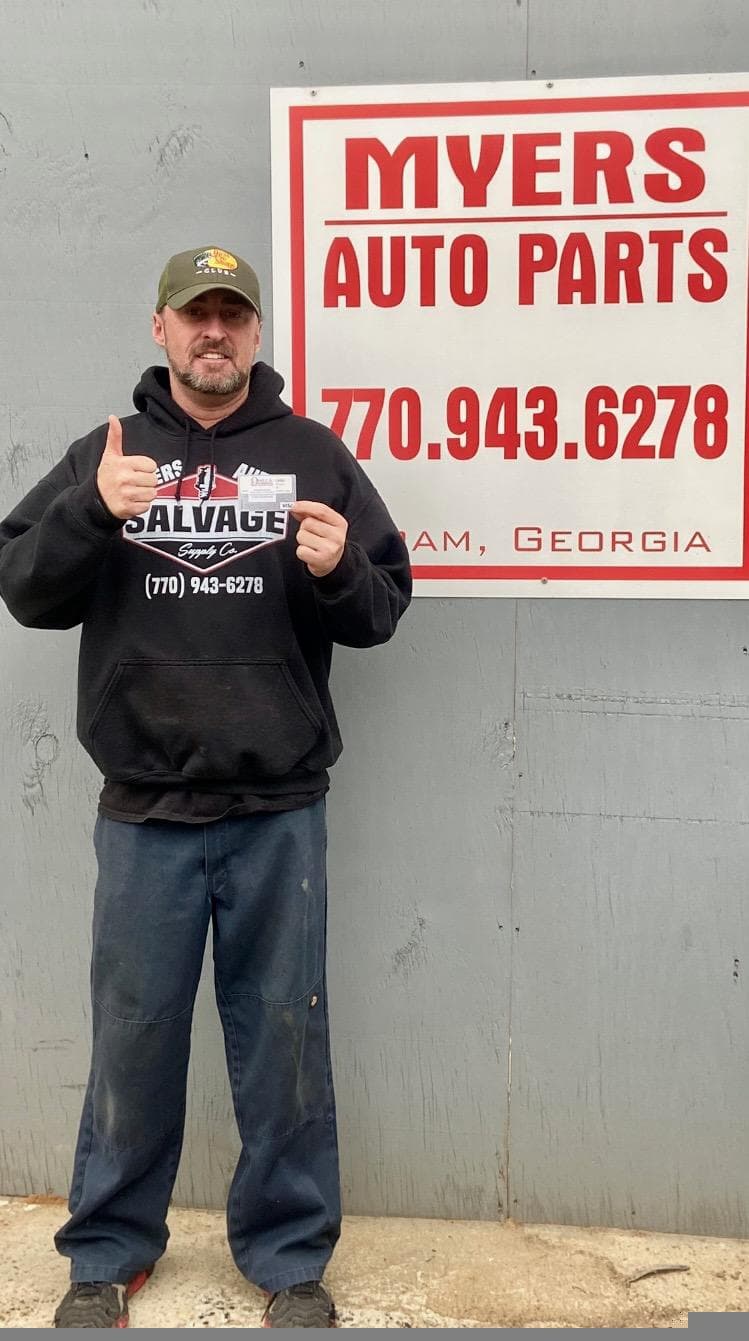 Auto parts merchant with rewards card in front of business signage, Omega rewards program, Acworth, Georgia