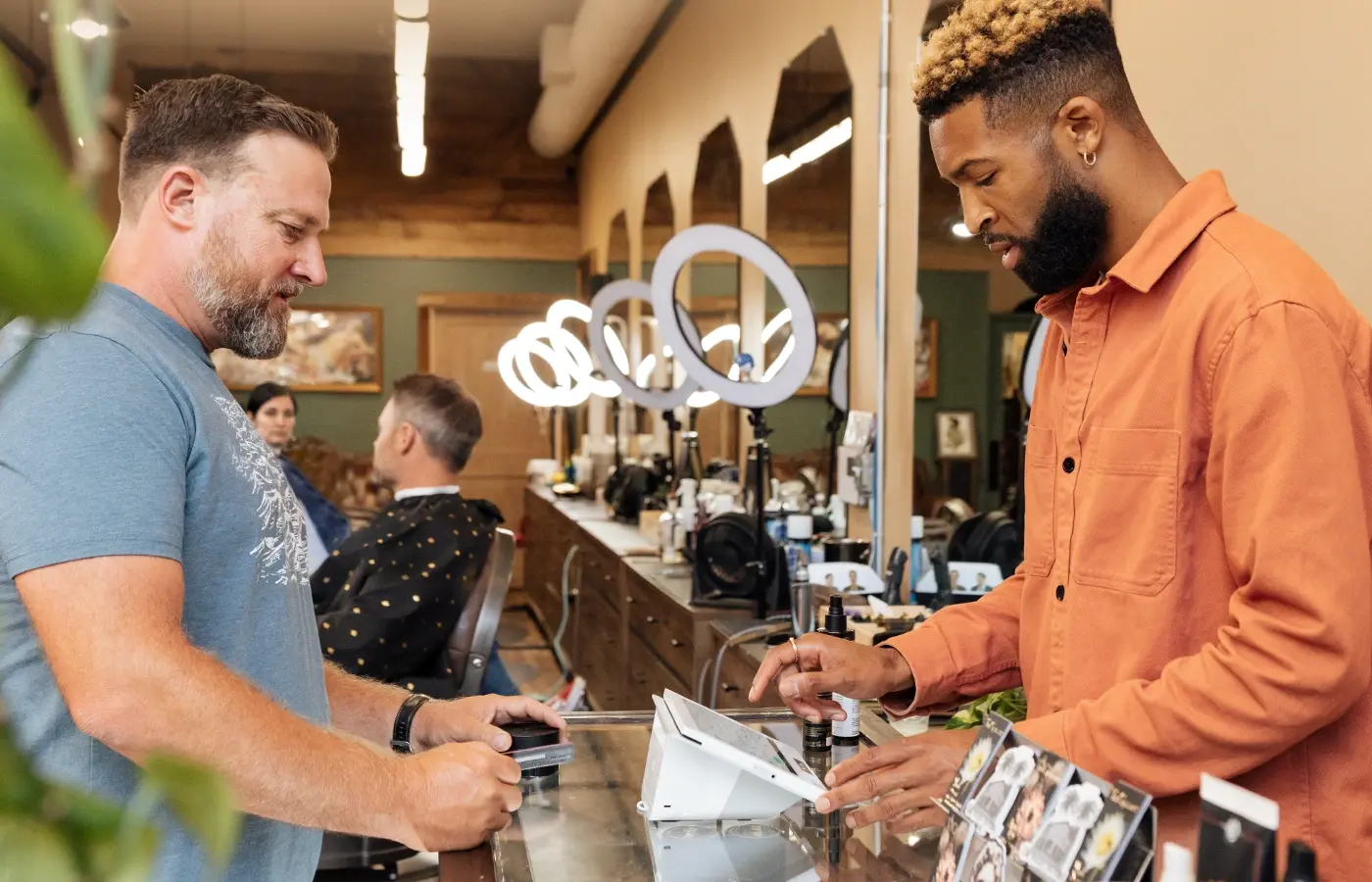 Shop owner using Clover Mini 3 at counter while customer pays in a modern barbershop