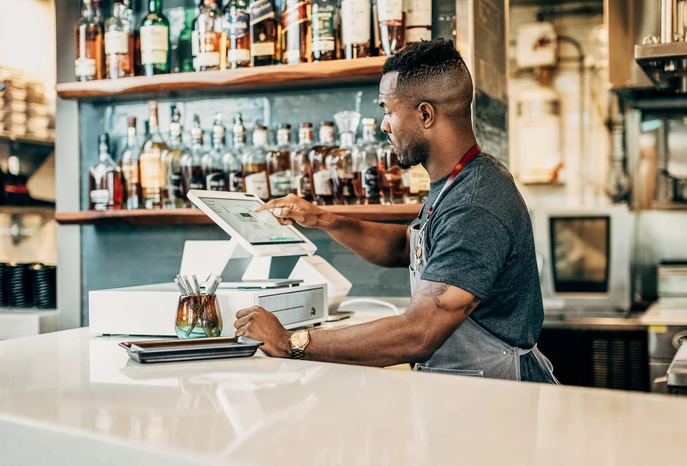 Bartender using Clover Station Solo behind a well-stocked bar with spirits on wooden shelves