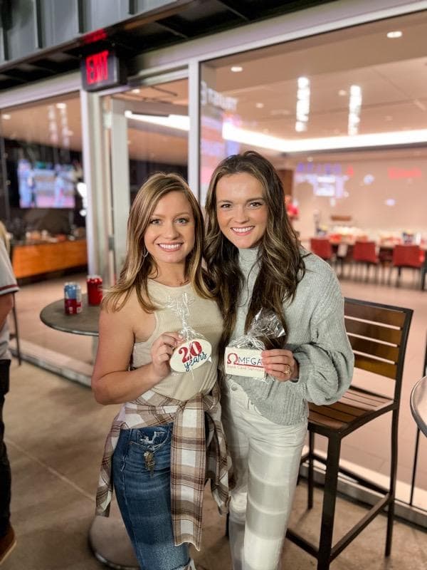 Omega team members Kenzi and Katie holding cookies celebrating twenty years and Omega Bank Card Services at a Braves game